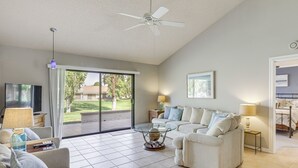 A spacious living room with a large glass door leading to a patio, a ceiling fan, and a flat-screen TV.