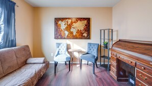 A living room with a brown sofa, two blue armchairs, a small round table, a wooden cabinet, and a world map artwork on the wall. - Private Yard & Patio: Fort Worth Family Home (Fort Worth)