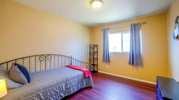 Une chambre à coucher avec un lit, une table de chevet, une lampe, une fenêtre avec des rideaux et un luminaire au plafond.