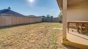 A backyard with a wooden fence, a patio with a table and chairs, and a clear sky. - Private Yard & Patio: Fort Worth Family Home (Fort Worth)