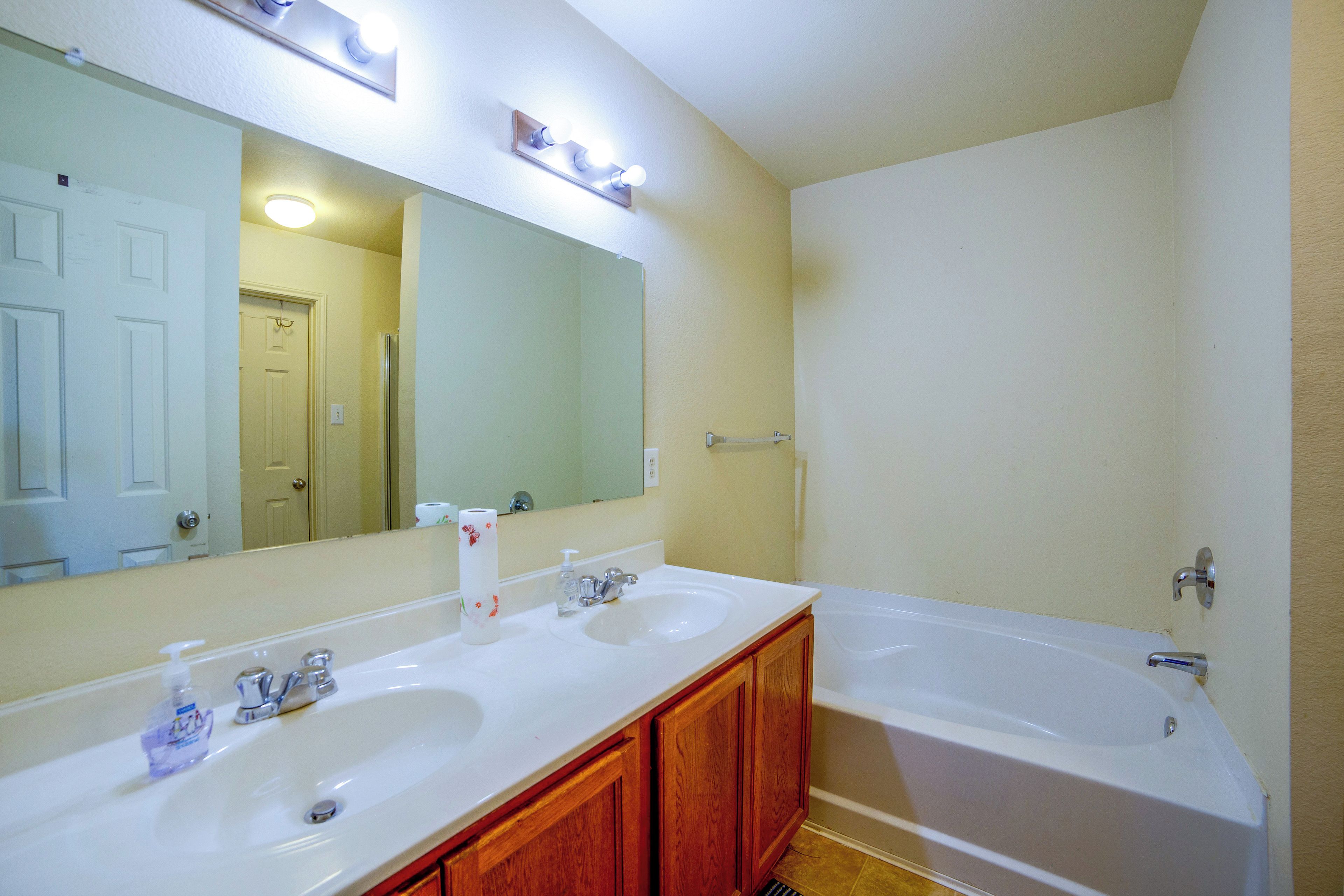 A bathroom with two sinks, a mirror, a bathtub, and a toilet.