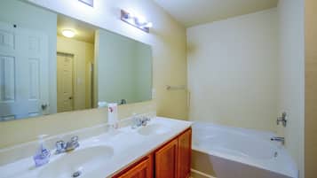 A bathroom with two sinks, a mirror, a bathtub, and a toilet.