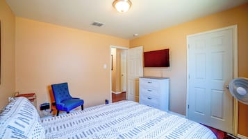 Un dormitorio con cama, una silla, cómoda, televisor y ventilador.