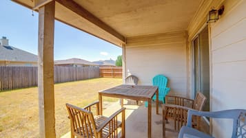 Un patio techado con mesa y sillas, una valla de madera y vistas a una zona residencial.