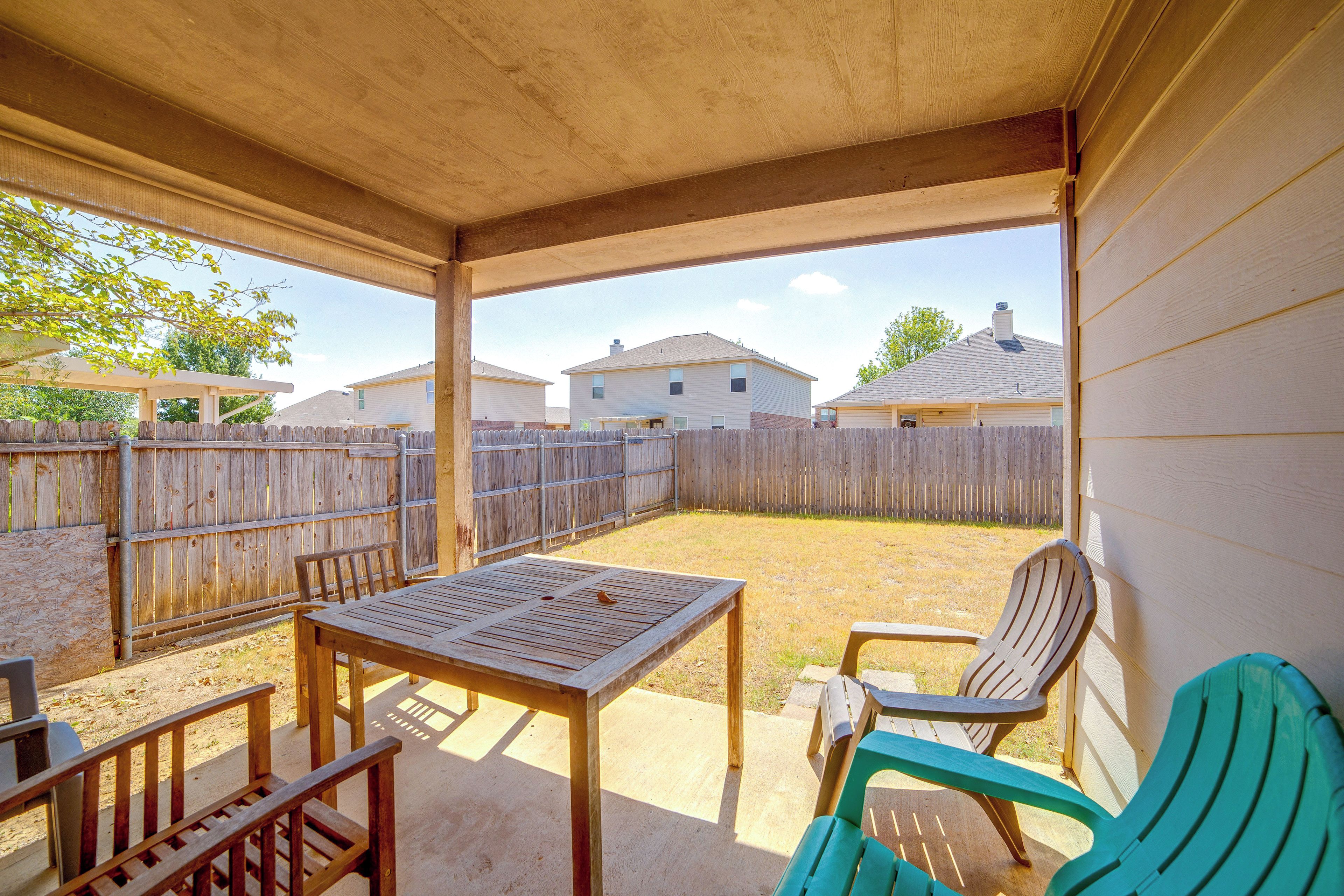 Un patio couvert avec une table et des chaises, une clôture en bois et des maisons en arrière-plan.