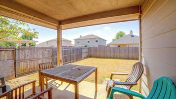 Un patio couvert avec une table et des chaises, une clôture en bois et des maisons en arrière-plan.