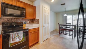 A kitchen with wooden cabinets, a black stove, a microwave, and a tiled backsplash. - Private Yard & Patio: Fort Worth Family Home (Fort Worth)