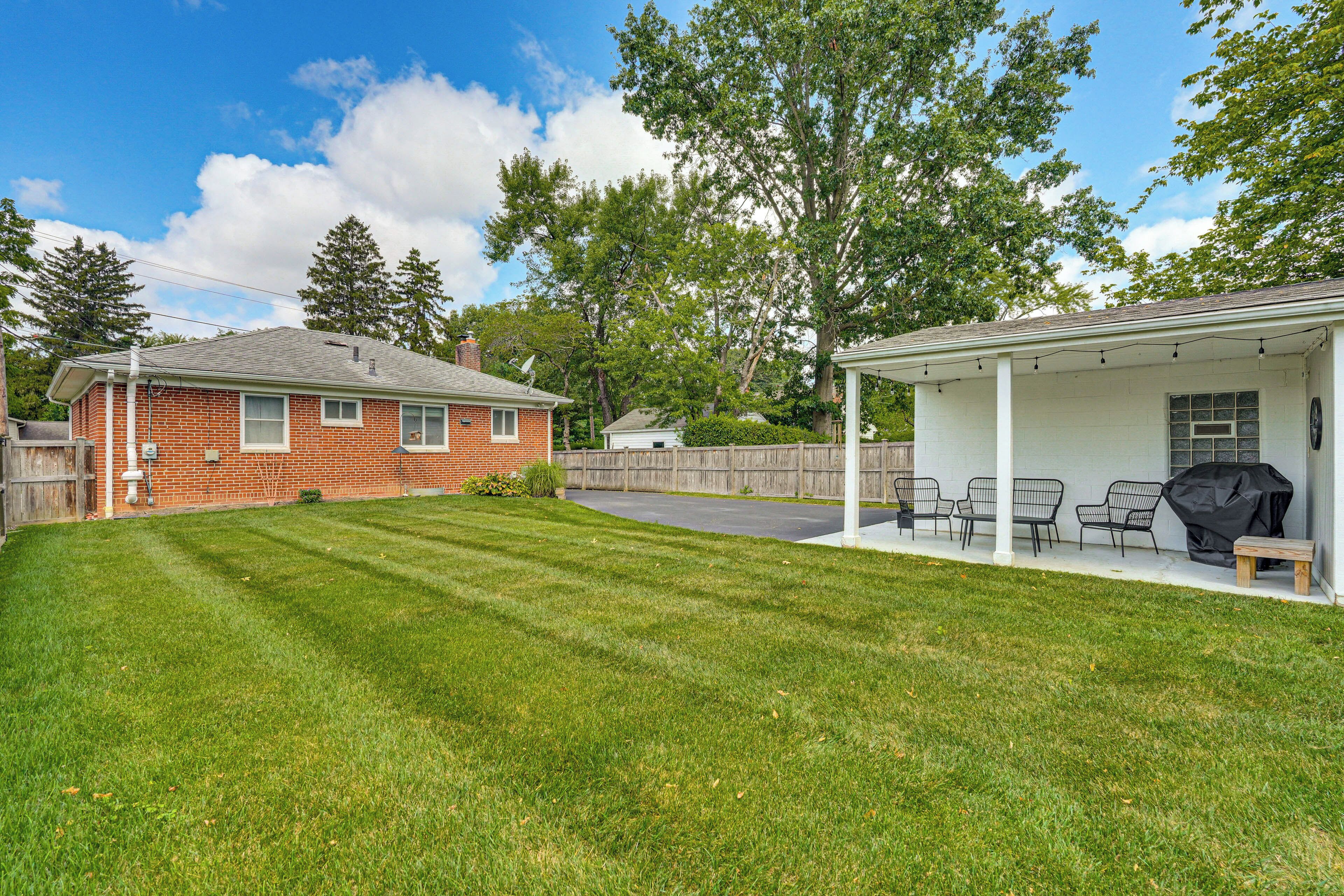 A backyard with a covered patio, a brick house, and a wooden fence.