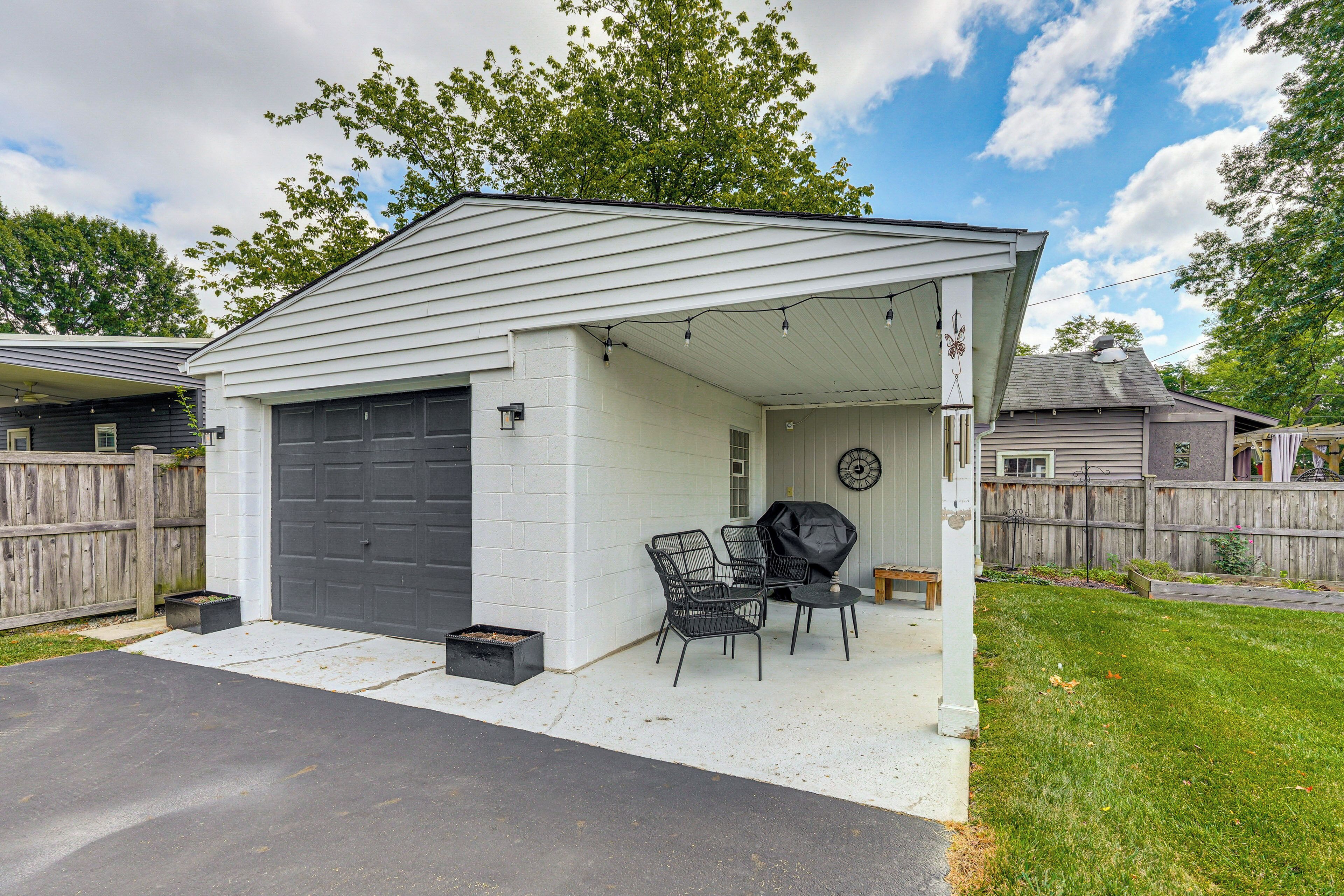 A covered patio with a grill, two chairs, and a table.