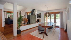 A spacious living area with a dining table, chairs, a large potted plant, and a fireplace. - Liiiving in Caminha Countryside Pool House (Caminha)