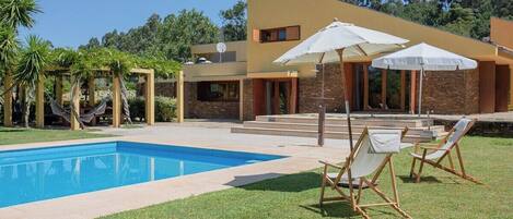 A modern house with a swimming pool, outdoor seating, and a garden.