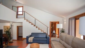 A spacious living area with a staircase, a blue sofa, a beige sofa, and wicker ottomans. - Liiiving in Caminha Countryside Pool House (Caminha)
