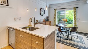 A modern kitchen with a white countertop, wooden cabinets, a built-in dishwasher, and a dining area with a table and chairs.