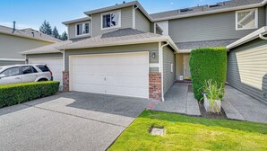 A two-story residential house with a garage, a well-maintained lawn, and a hedge.