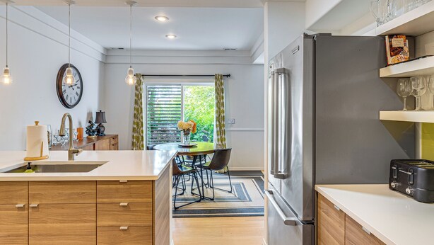 A modern kitchen with wooden cabinets, a stainless steel refrigerator, and a dining area with a table and chairs.