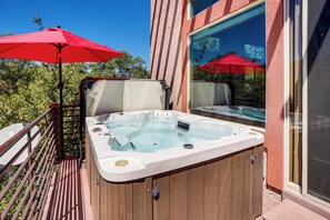 A wooden hot tub with a glass enclosure, red umbrellas, and a wooden deck.