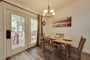 A dining area with a wooden table set for four, surrounded by rustic chairs, a chandelier, and a framed picture on the wall.