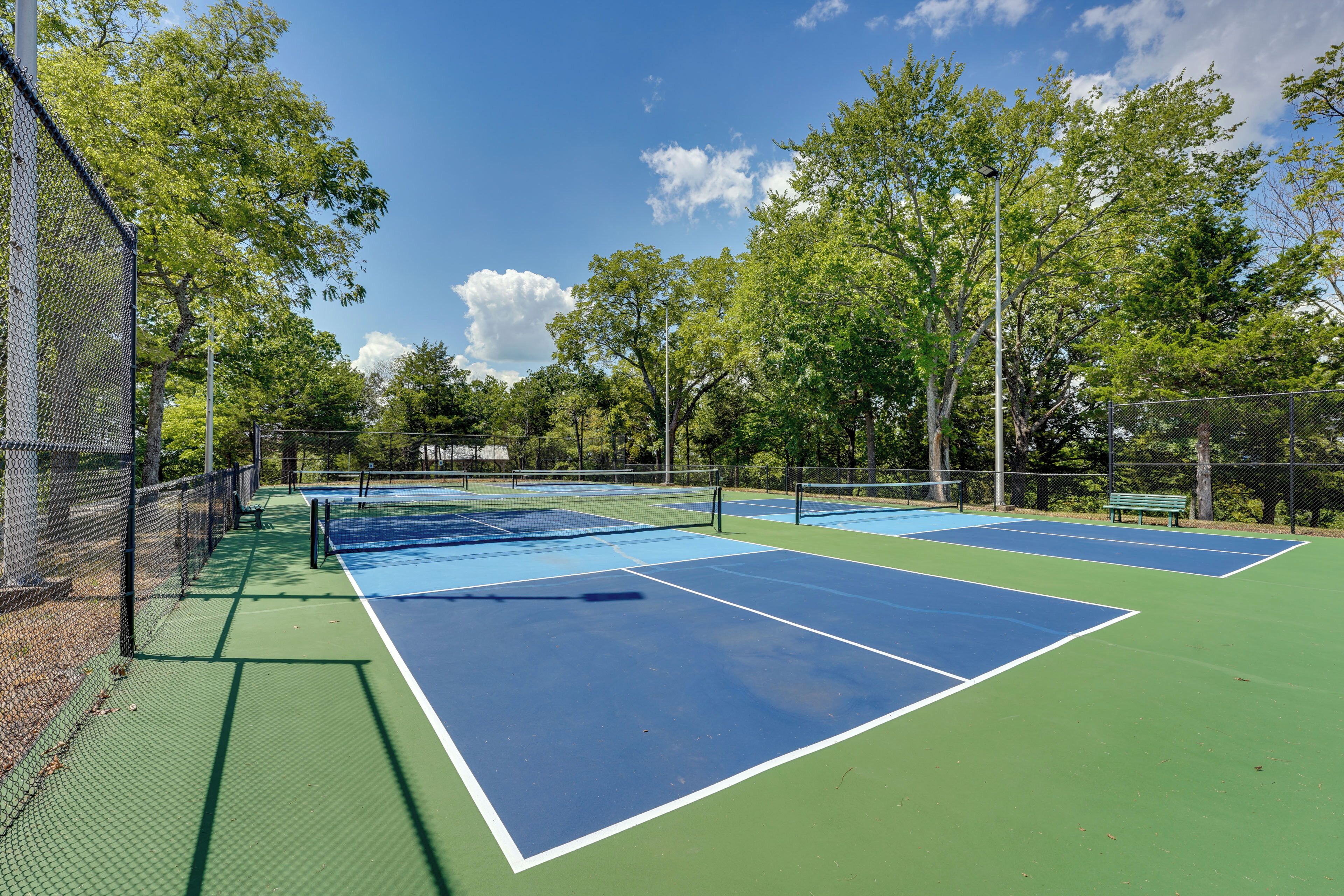Un campo da tennis all'aperto con più campi, circondato da alberi e una recinzione.