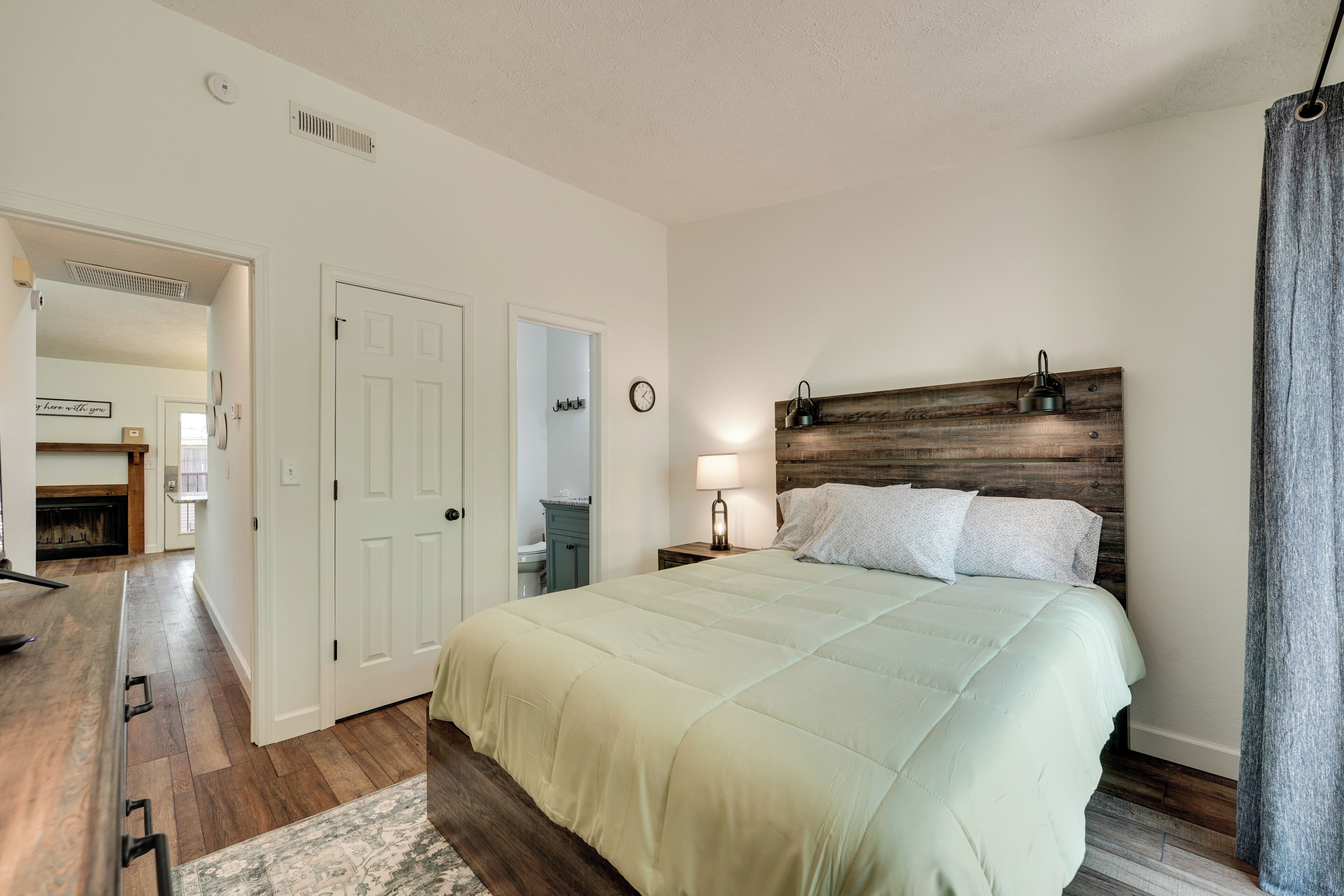 Une chambre à coucher comprenant un lit, une table de chevet, une horloge murale et une porte donnant sur une autre pièce.