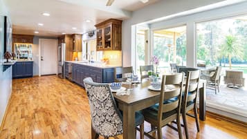 Uma cozinha espaçosa com armários de madeira, uma área de jantar com mesa e cadeiras, e grandes janelas com vista para o exterior.