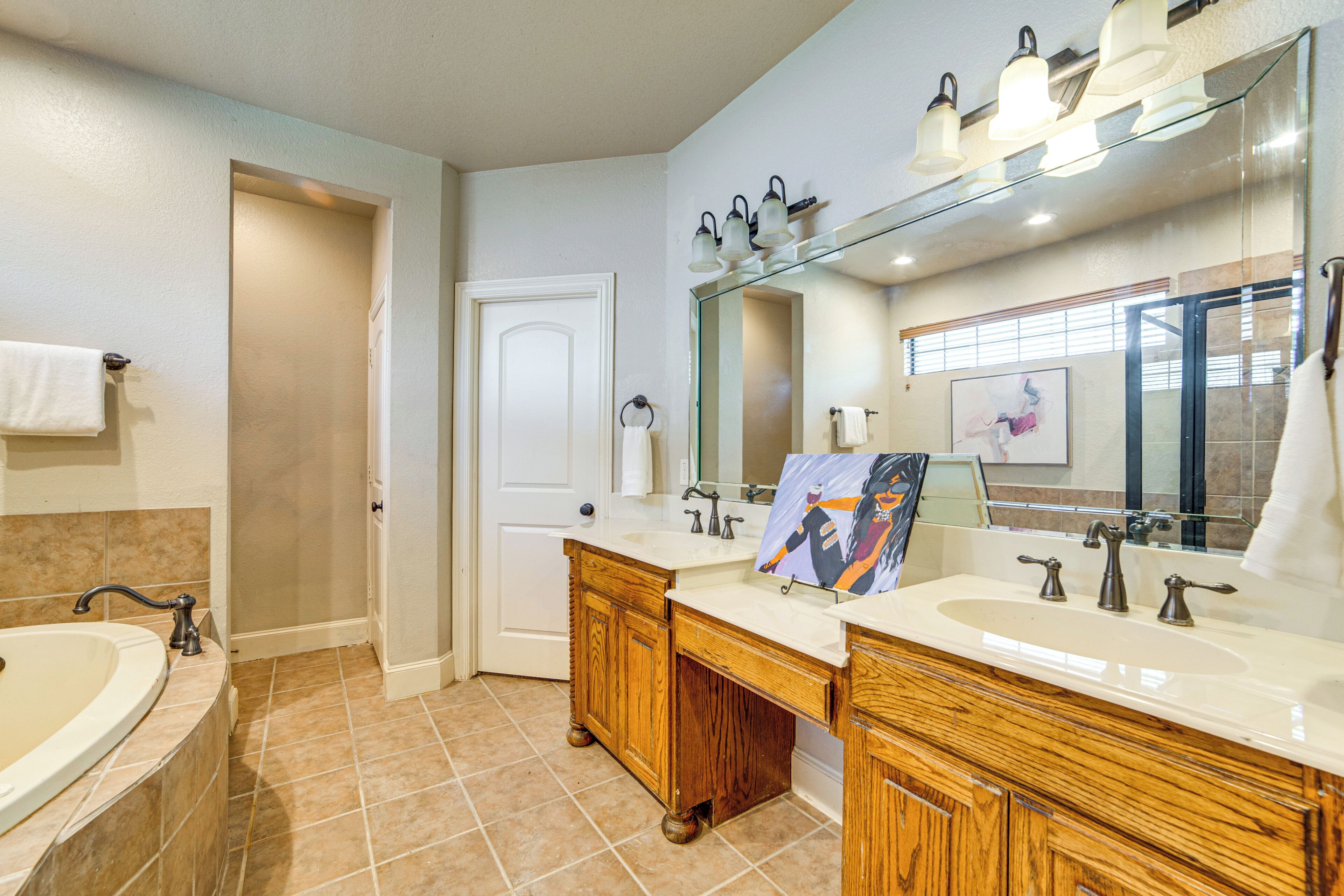 A bathroom with two sinks, a bathtub, wooden cabinets, a large mirror, and a painting on the wall.