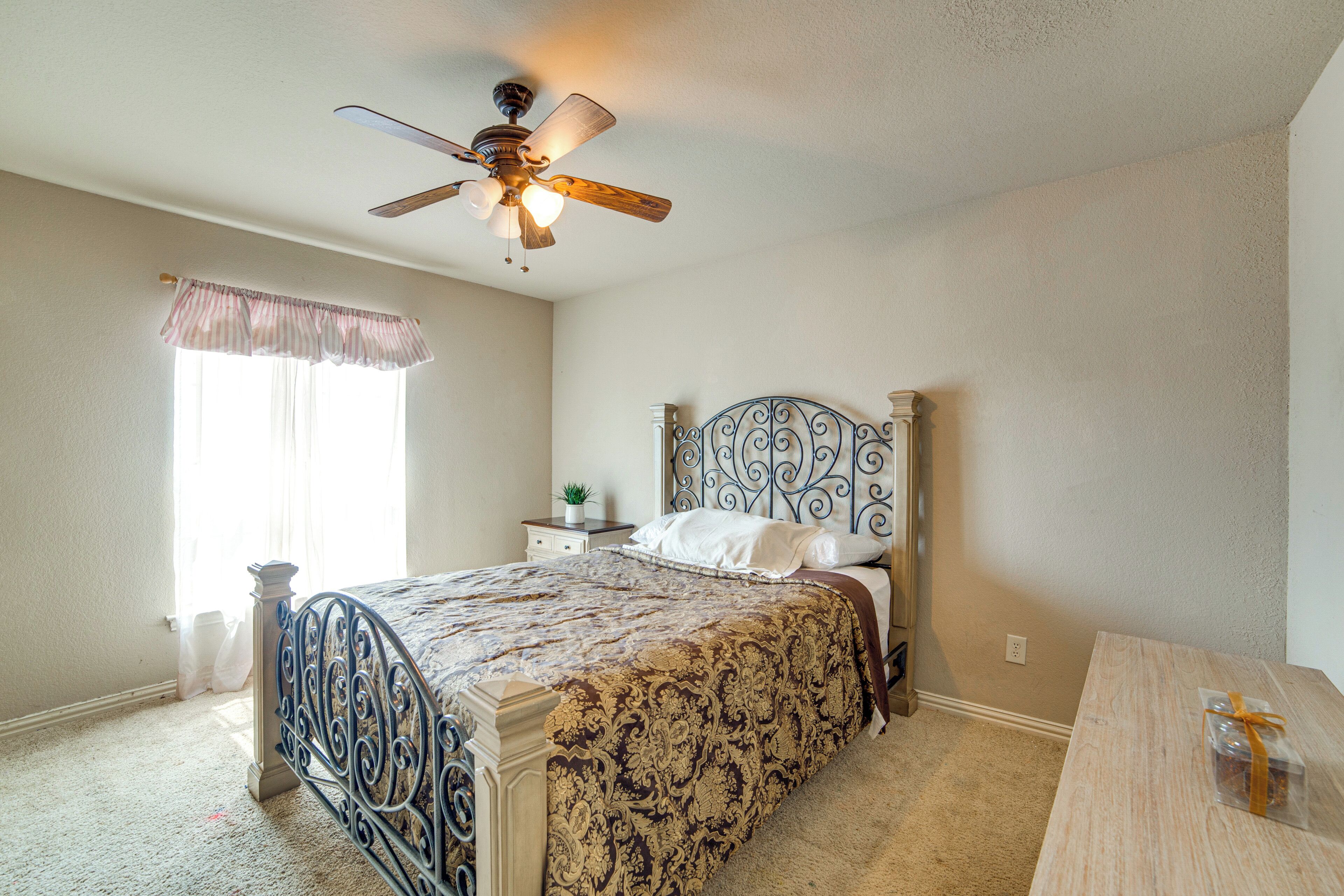 A bedroom with a bed, a ceiling fan, a nightstand, and a window with curtains.