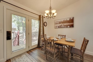 A dining area with a wooden table set for four, surrounded by rustic chairs, a chandelier, and a framed picture on the wall. - 3 Mi to Table Rock Lake: Cozy Cabin in the Woods! (Kimberling City)