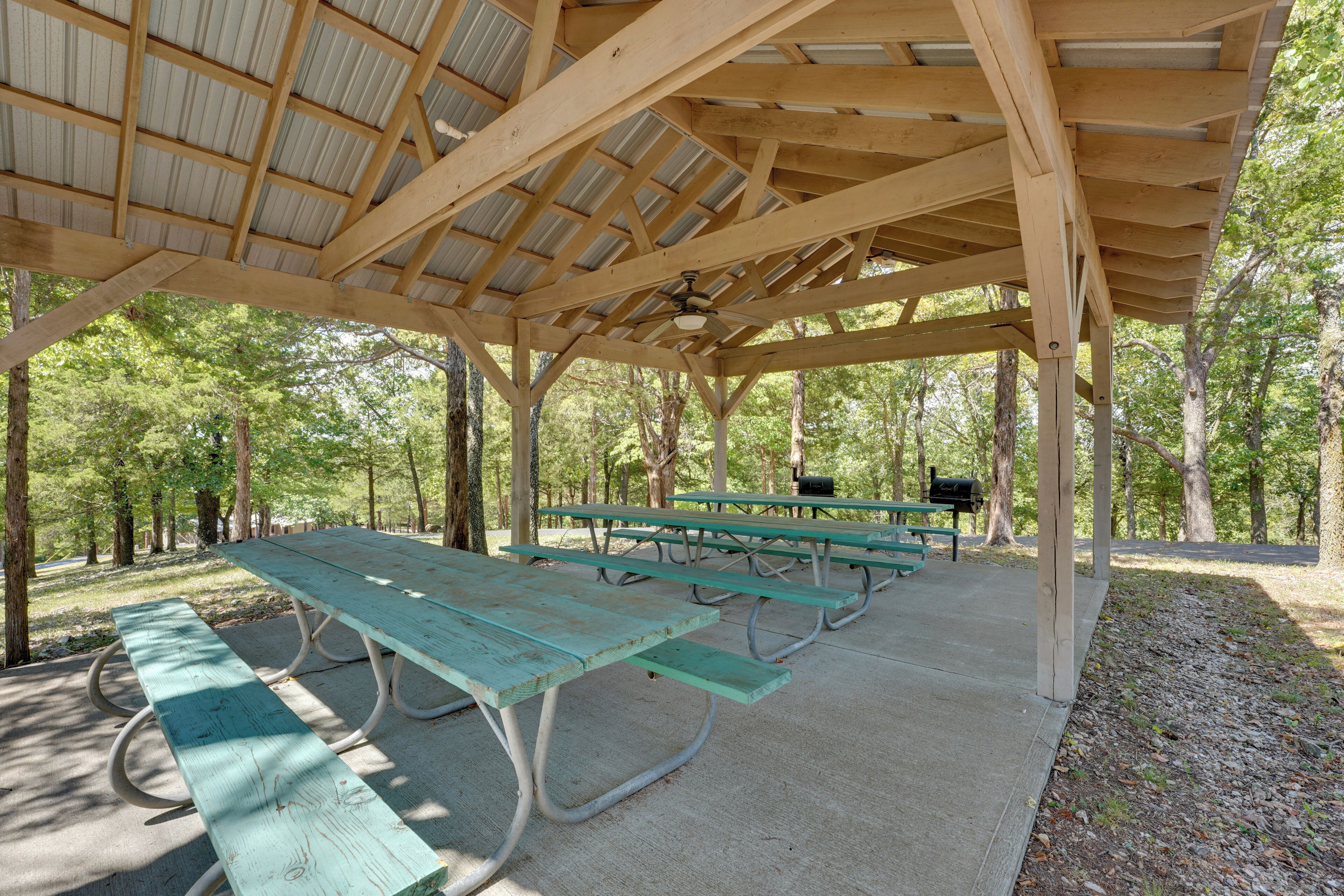 A covered picnic area with multiple picnic tables and benches, surrounded by trees.