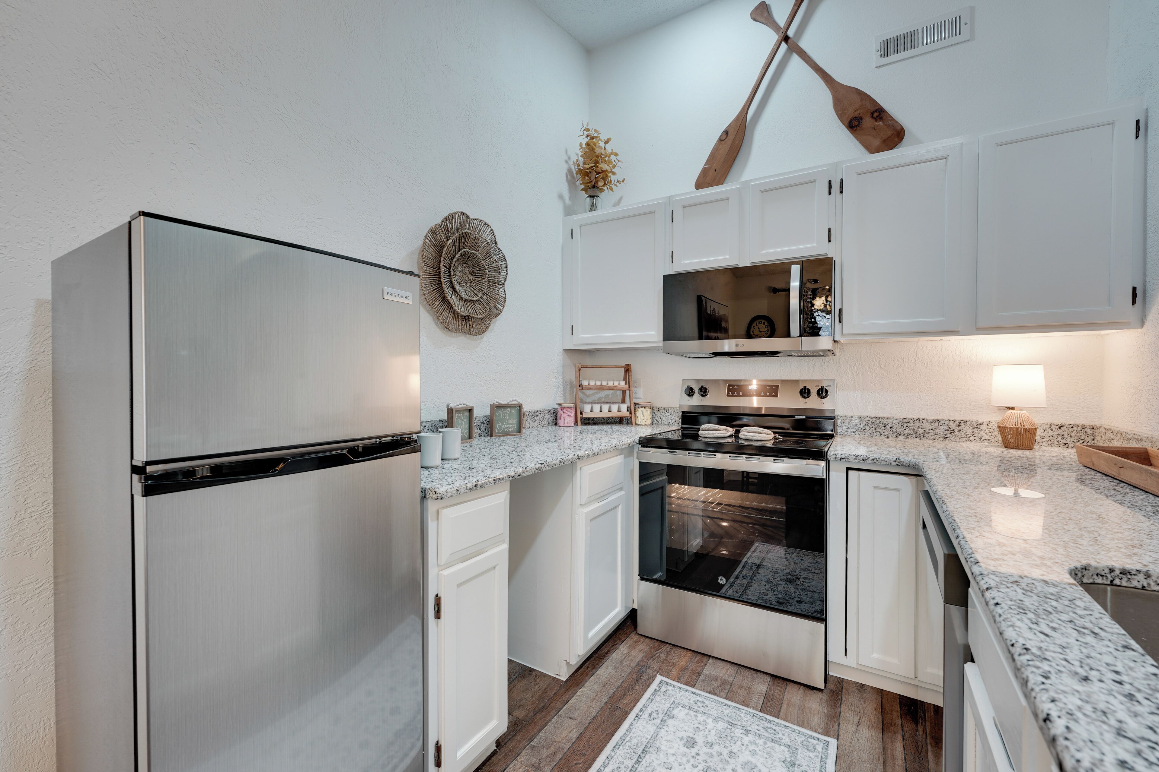 A modern kitchen with white cabinets, stainless steel appliances, and a wooden floor.