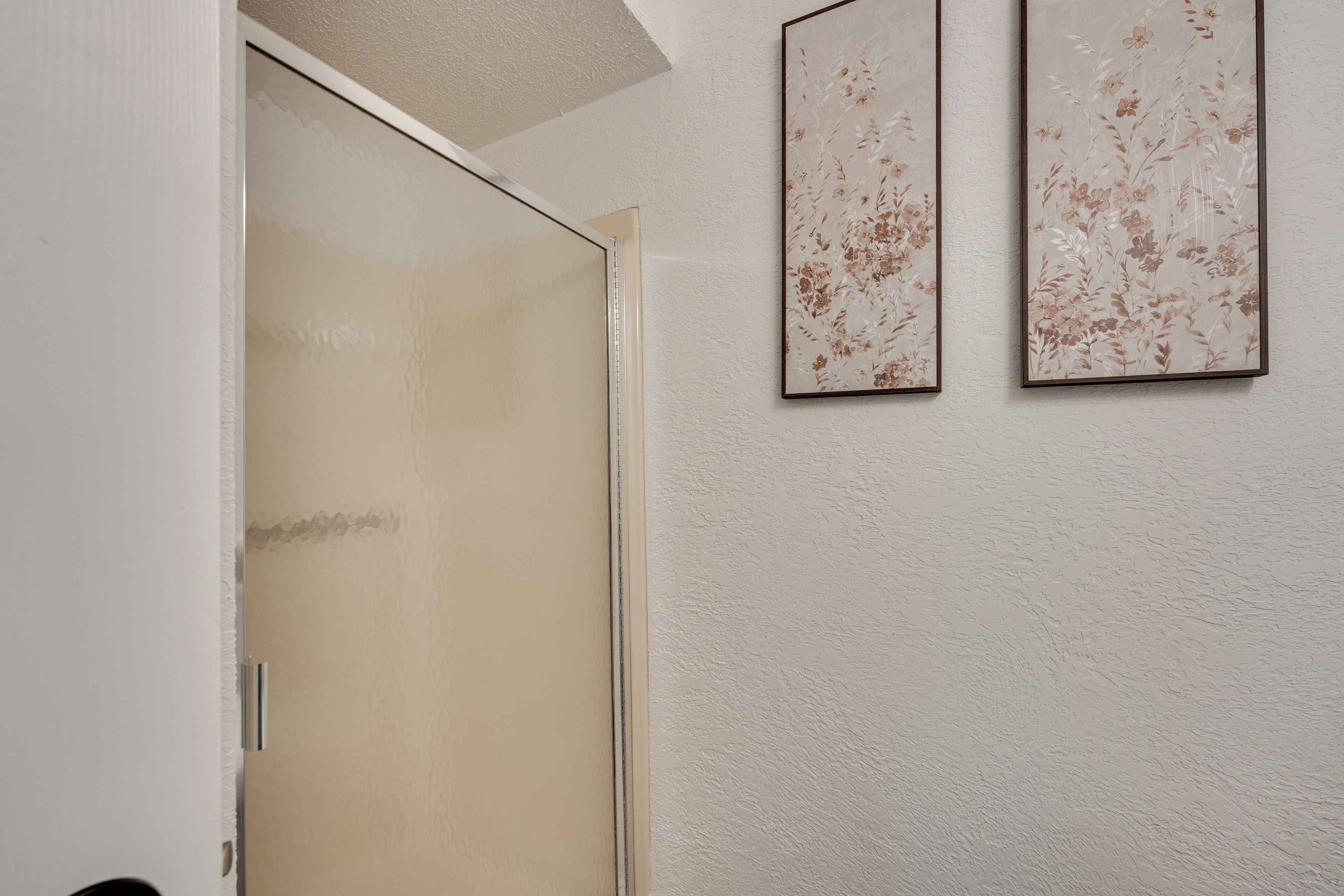 Una habitación con puerta corredera, pared con textura y dos cuadros de motivos florales.
