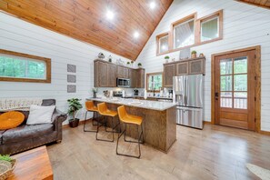 A modern kitchen with wooden cabinets, a large island with bar stools, a refrigerator, and a microwave. - Fire Pit & Hot Tub: Couples Retreat in Broken Bow (Broken Bow)