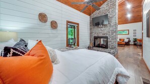 A bedroom with a large bed, a stone fireplace, and a ceiling fan. - Fire Pit & Hot Tub: Couples Retreat in Broken Bow (Broken Bow)