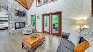 A cozy living room with a stone fireplace, a comfortable sofa, and a wooden coffee table. - Fire Pit & Hot Tub: Couples Retreat in Broken Bow (Broken Bow)