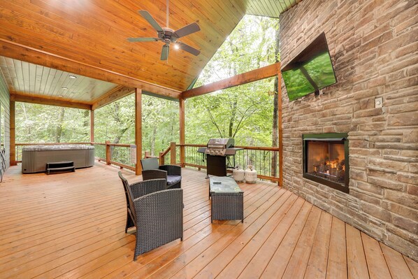 Una terraza techada con chimenea de piedra, mobiliario exterior y un jacuzzi.