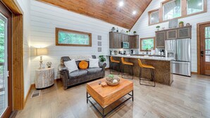 A spacious kitchen with wooden cabinets, a central island, and a dining area with bar stools. - Fire Pit & Hot Tub: Couples Retreat in Broken Bow (Broken Bow)