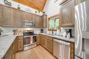 Una cocina con armarios de madera, electrodomésticos de acero inoxidable, encimeras de granito y una ventana con vistas al verdor.