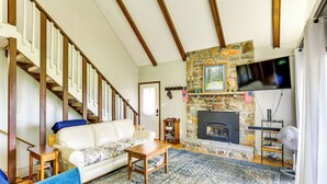 A living room with a fireplace, a sofa, a coffee table, and a television mounted on the wall. - Deck, Fire Pit, Games: Family Escape Near Boone (Zionville)