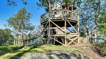 A wooden observation tower with a slide, surrounded by trees and a clear sky.