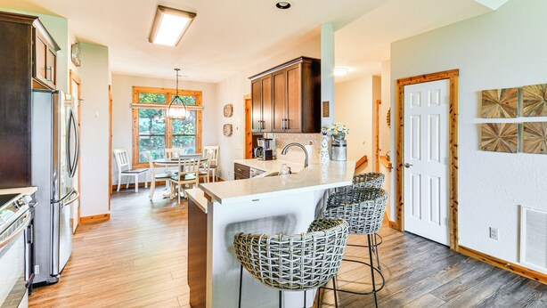 A modern kitchen with a central island, bar stools, and a dining area with a view of the outdoors. - 6 Mi to Pisgah Nat'l Forest! Condo w/ Serene Views (Burnsville)