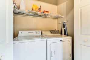 A laundry room with a front-loading washer and dryer, a shelf with various items, and a door to the right. - Stunning Blue Ridge Views & Modern Mountain Ease (Burnsville)