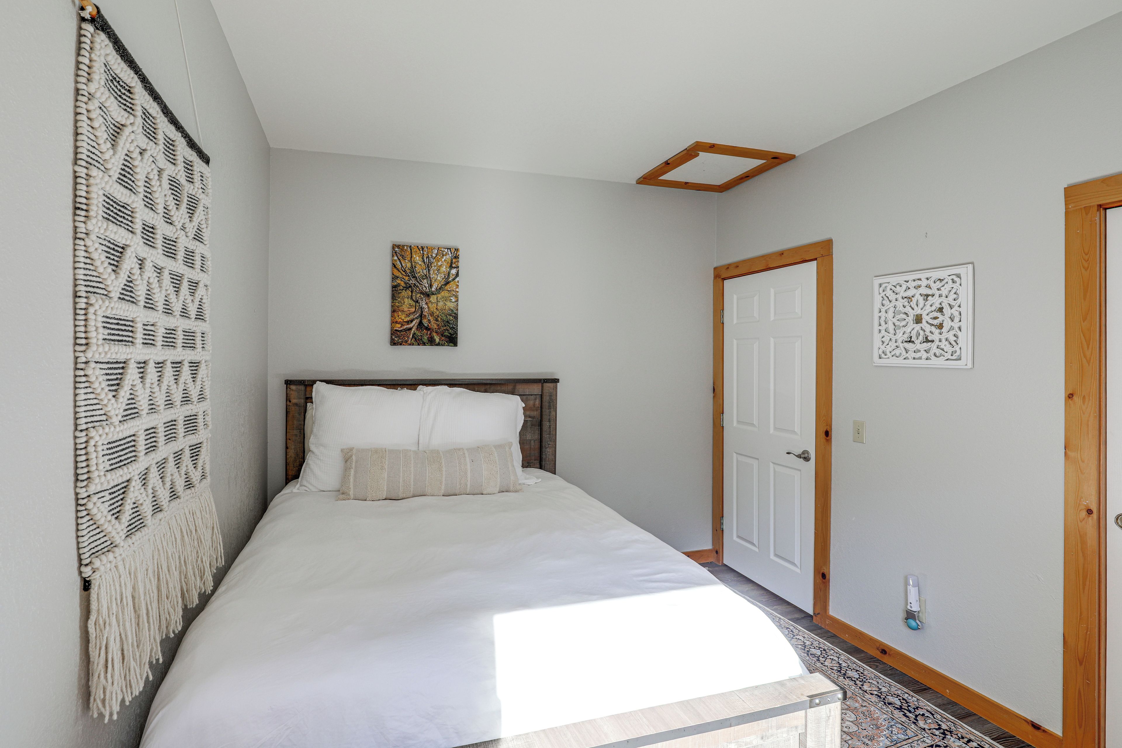 A bedroom with a bed, a wall-mounted painting, a door, and a macrame wall hanging.