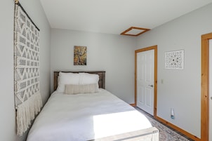 Un dormitorio con cama, un cuadro en la pared, una puerta y un adorno de macramé.