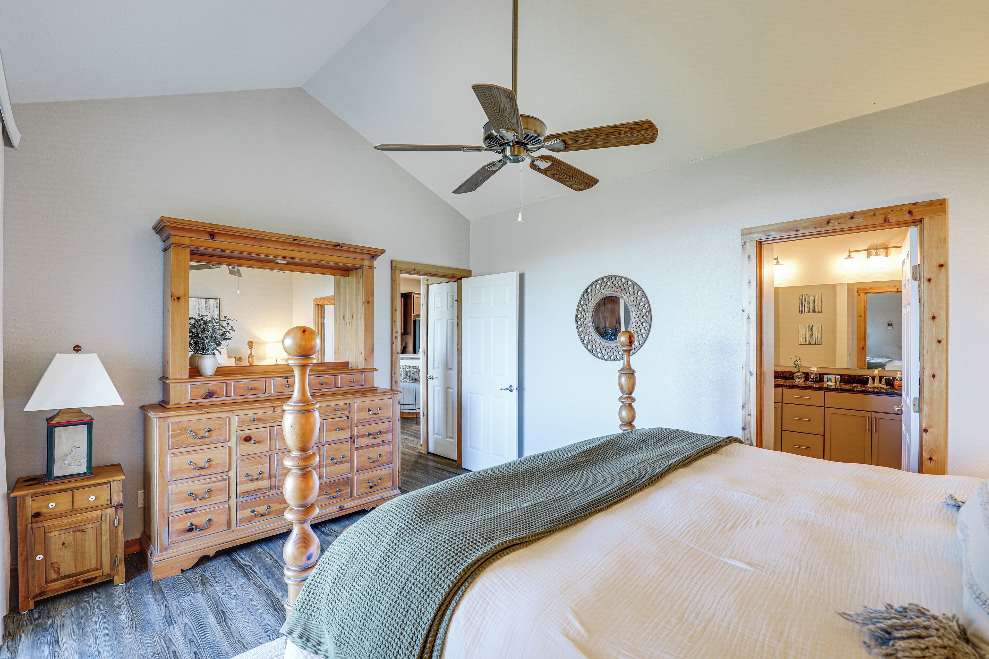 A bedroom with a bed, dresser, mirror, ceiling fan, and a bathroom visible through an open door.