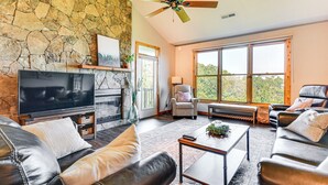 A living room with a stone wall, a fireplace, a television, leather sofas, and large windows offering a view of the outdoors. - 6 Mi to Pisgah Nat'l Forest! Condo w/ Serene Views (Burnsville)