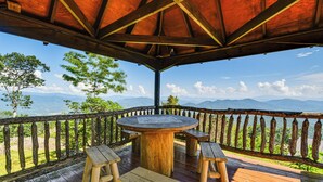 A wooden deck with a round table and benches, overlooking a mountainous landscape. - 6 Mi to Pisgah Nat'l Forest! Condo w/ Serene Views (Burnsville)