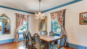 A dining room with a wooden table and chairs, blue patterned curtains, and a chandelier. - Historic Waterfront Home w/ Dock in Reedville! (Reedville)