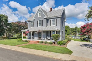 Uma casa de dois andares com varanda frontal, chaminé e um mastro com a bandeira americana.
