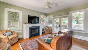 A living room with a fireplace, leather sofa, armchair, and a flat-screen TV mounted above the fireplace. - Historic Waterfront Home w/ Dock in Reedville! (Reedville)