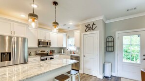 A modern kitchen with stainless steel appliances, a marble island with bar stools, and a large window providing natural light. - Walk to Lake Martin: Water-view Retreat w/ Deck! (Tallassee)