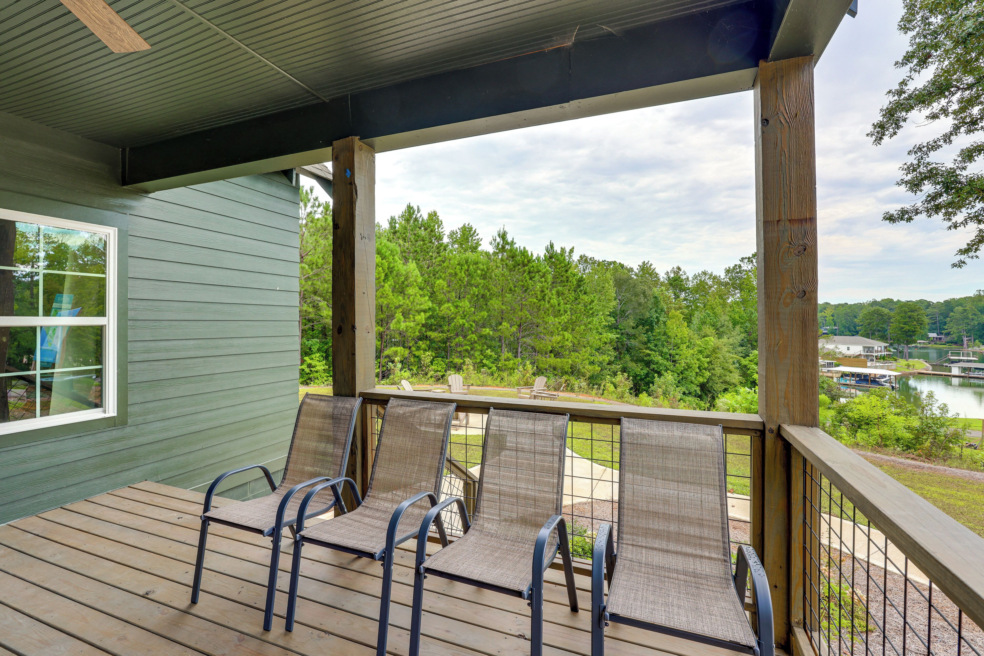 A covered deck with four chairs and a table, overlooking a lake and trees.